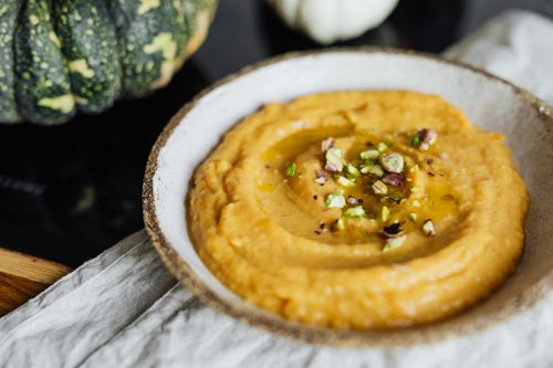 Free Close-up of creamy pumpkin hummus topped with pistachios in a rustic bowl. Stock Photo