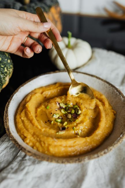 Small bowls of smooth orange sweet potato puree and green pea puree next to a baby spoon and ice cube tray of frozen portions.