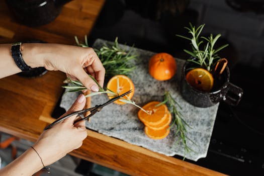 A close-up of hands cutting fresh rosemary next to sliced oranges on a kitchen countertop, ideal for culinary themes.