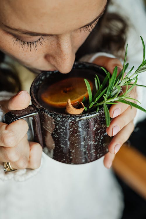 Woman Drinking Drink with Leaves, Cinnamon and Orange Slices