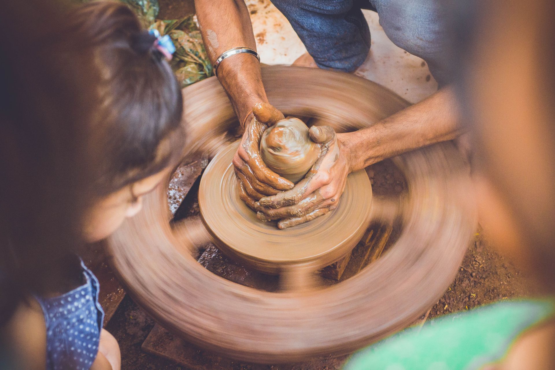 Hands shaping a wet clay bowl on a worktable beside pottery tools