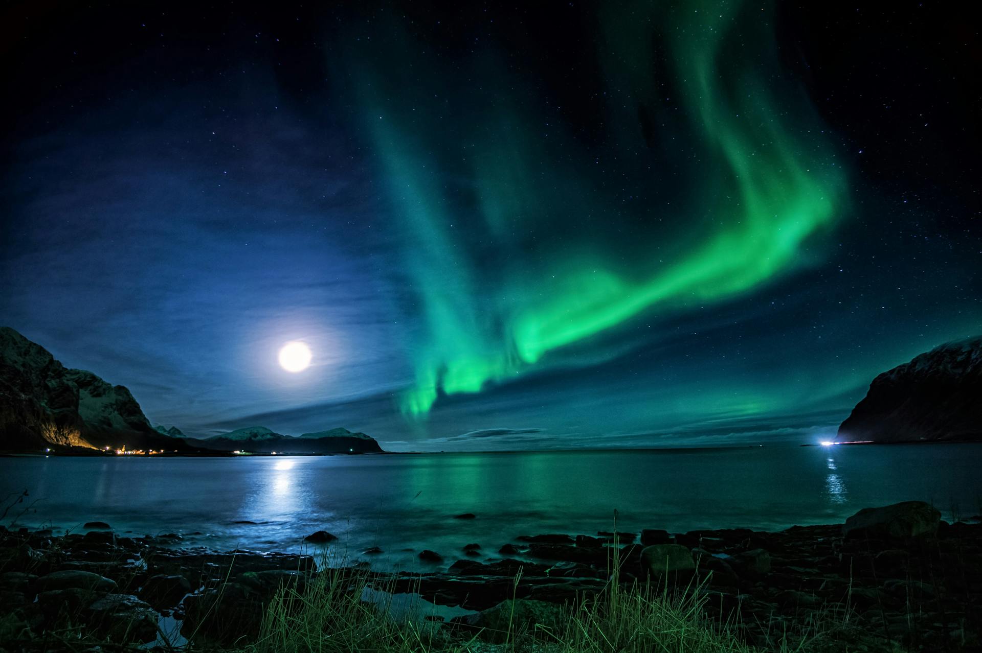 Scenic view of glowing sun with aurora in sky reflecting in sea near mountains at dusk