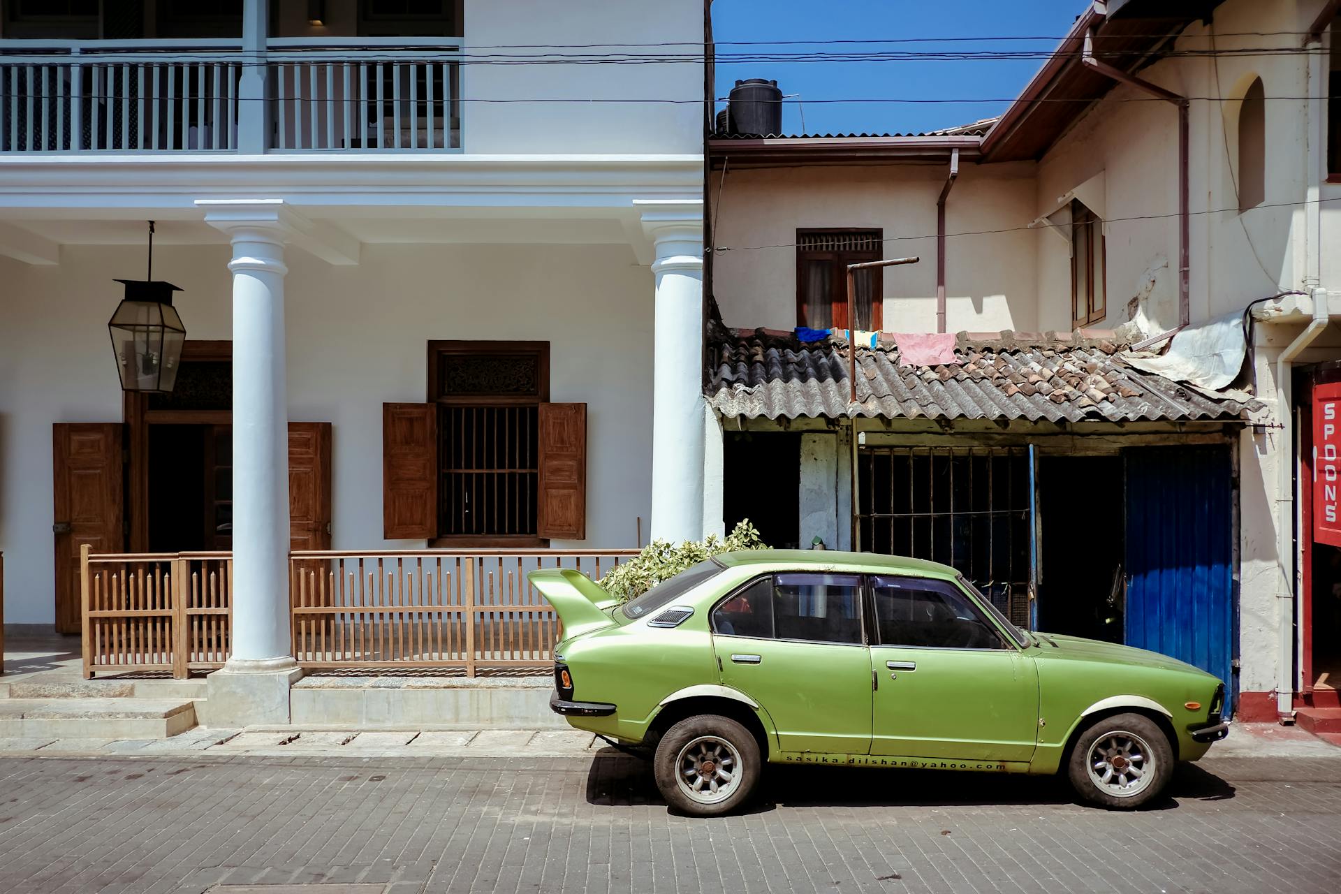 A classic green car parked on a street in Sri Lanka with colonial architecture.