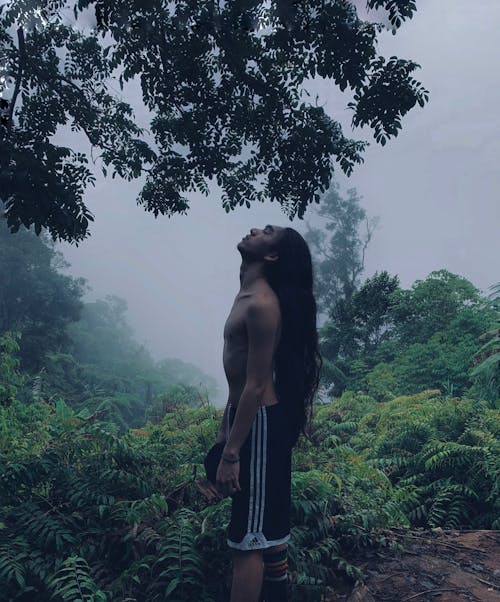 Young ethnic man resting in lush tropical forest on foggy day