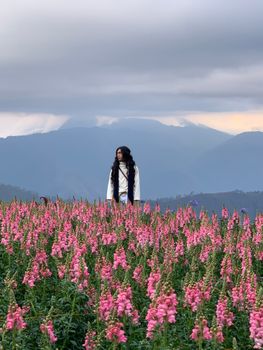 一名妇女安详地站在粉红色的田野里，背景是山脉