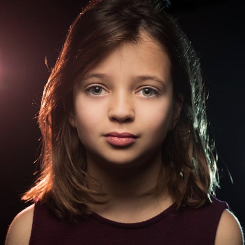 Little girl with green eyes standing in dark studio