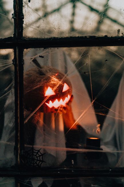A haunting Halloween scene with illuminated jack-o'-lanterns viewed through a spiderwebbed window.