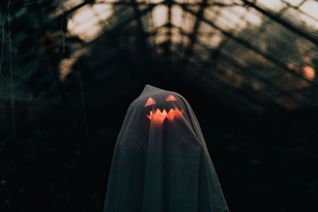 a ghostly figure with a glowing pumpkin face under a sheet in an eerie