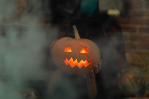 Free A glowing jack-o'-lantern held in hands surrounded by eerie smoke, perfect for Halloween. Stock Photo