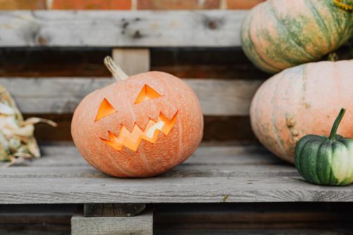 Free A glowing jack-o'-lantern on a rustic bench with additional pumpkins, perfect for Halloween decor. Stock Photo
