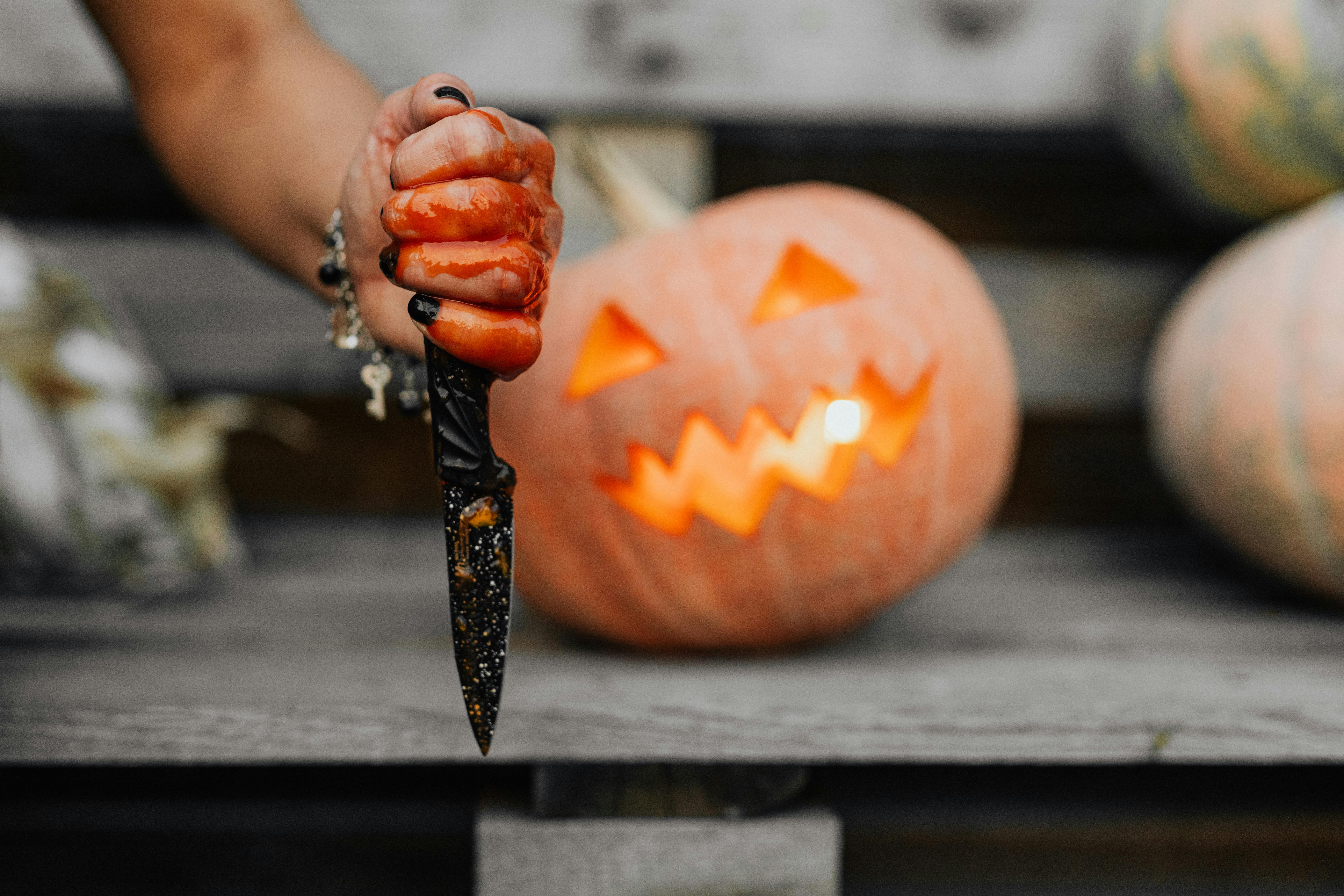 A bloodied hand holding a knife with a carved pumpkin in the background, perfect for Halloween.