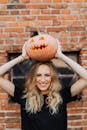 一名金发女子靠在砖墙上，高兴地将南瓜灯举过头顶