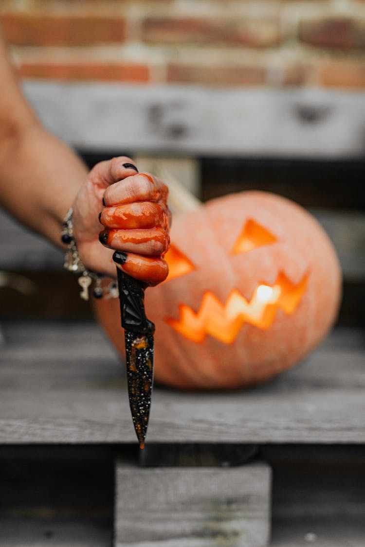 Hand With Knife Against Pumpkin Carved For Halloween