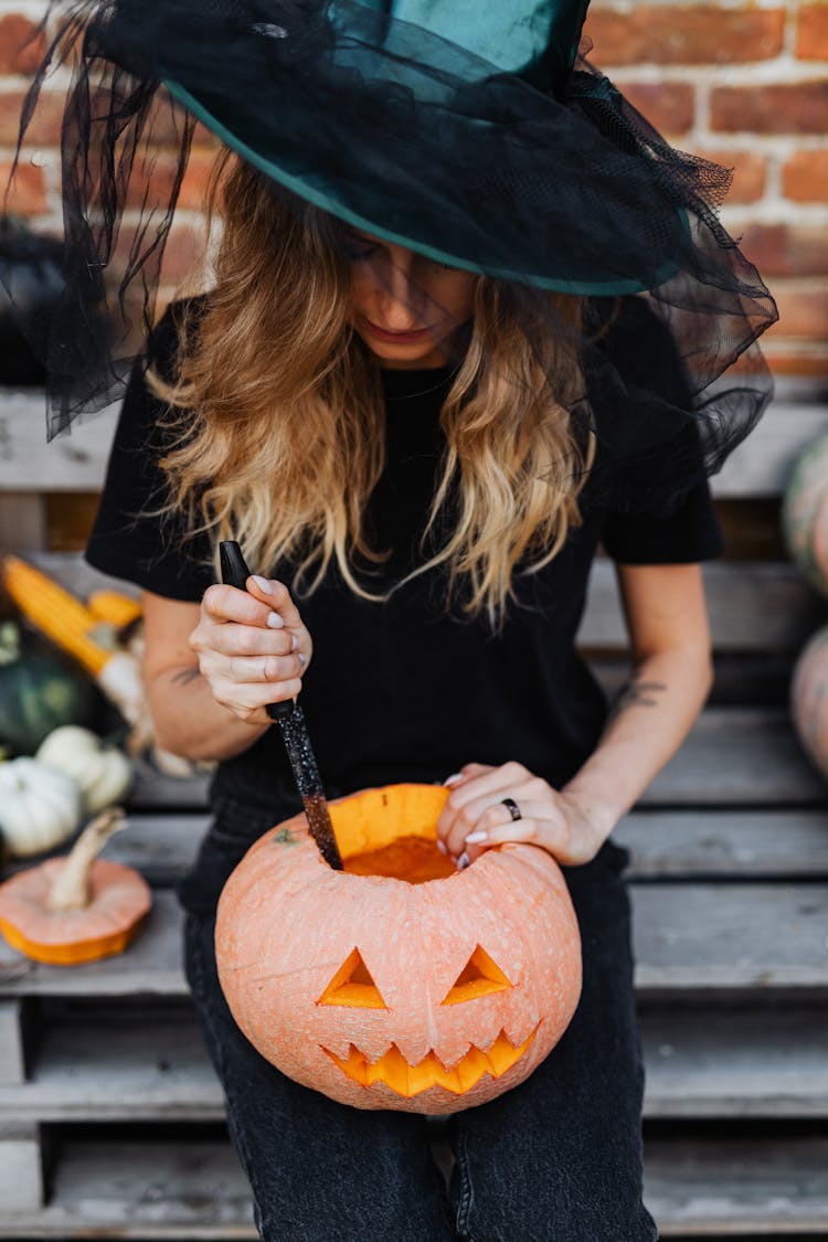 Woman Wearing A Witch Hat Carving A Pumpkin For Halloween 