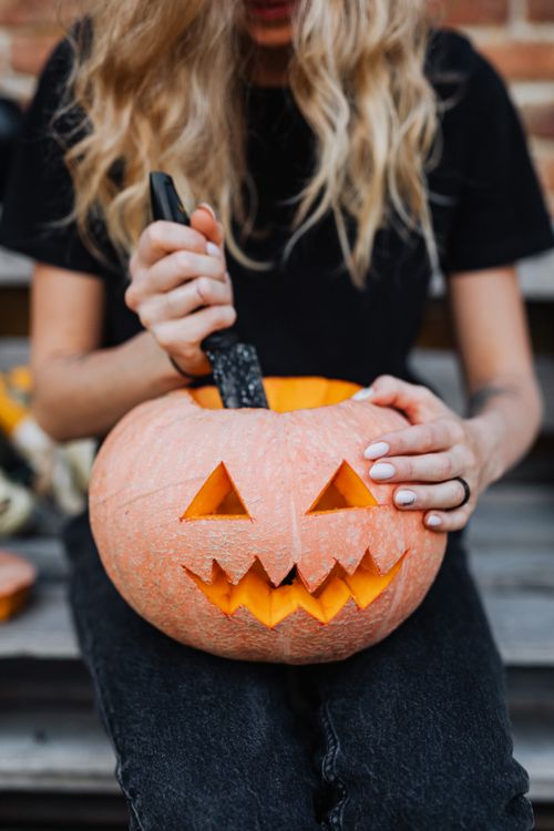 Free A woman skillfully carving a jack-o-lantern outdoors, capturing the Halloween spirit. Stock Photo