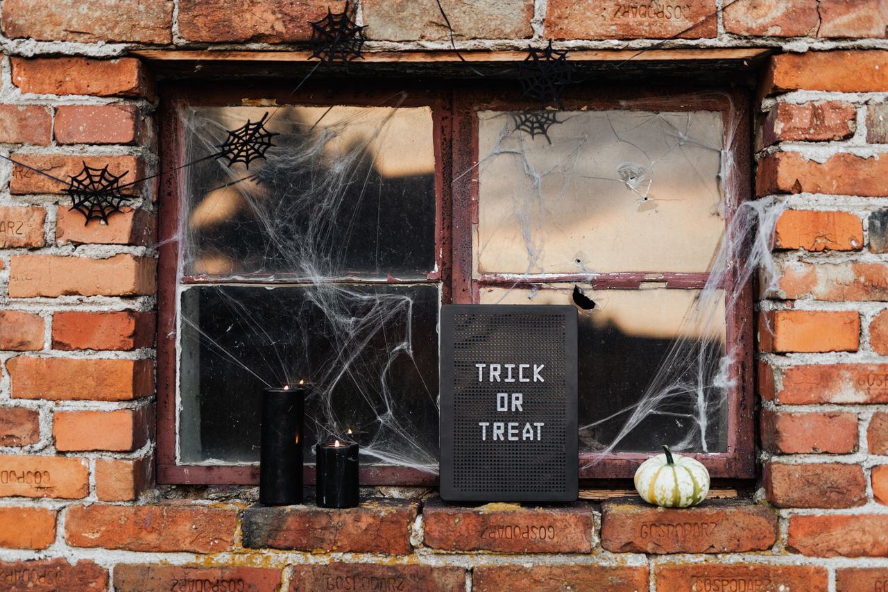 Brick window decorated with cobwebs, spiders, a Trick or Treat letter board, black candles, and a white pumpkin