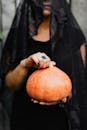 一位戴着面纱、穿着黑色连衣裙、手拿南瓜的女人的特写，非常适合万圣节主题