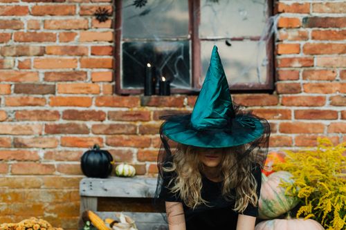 Free Woman in witch hat sitting outdoors against brick wall with pumpkins. Stock Photo