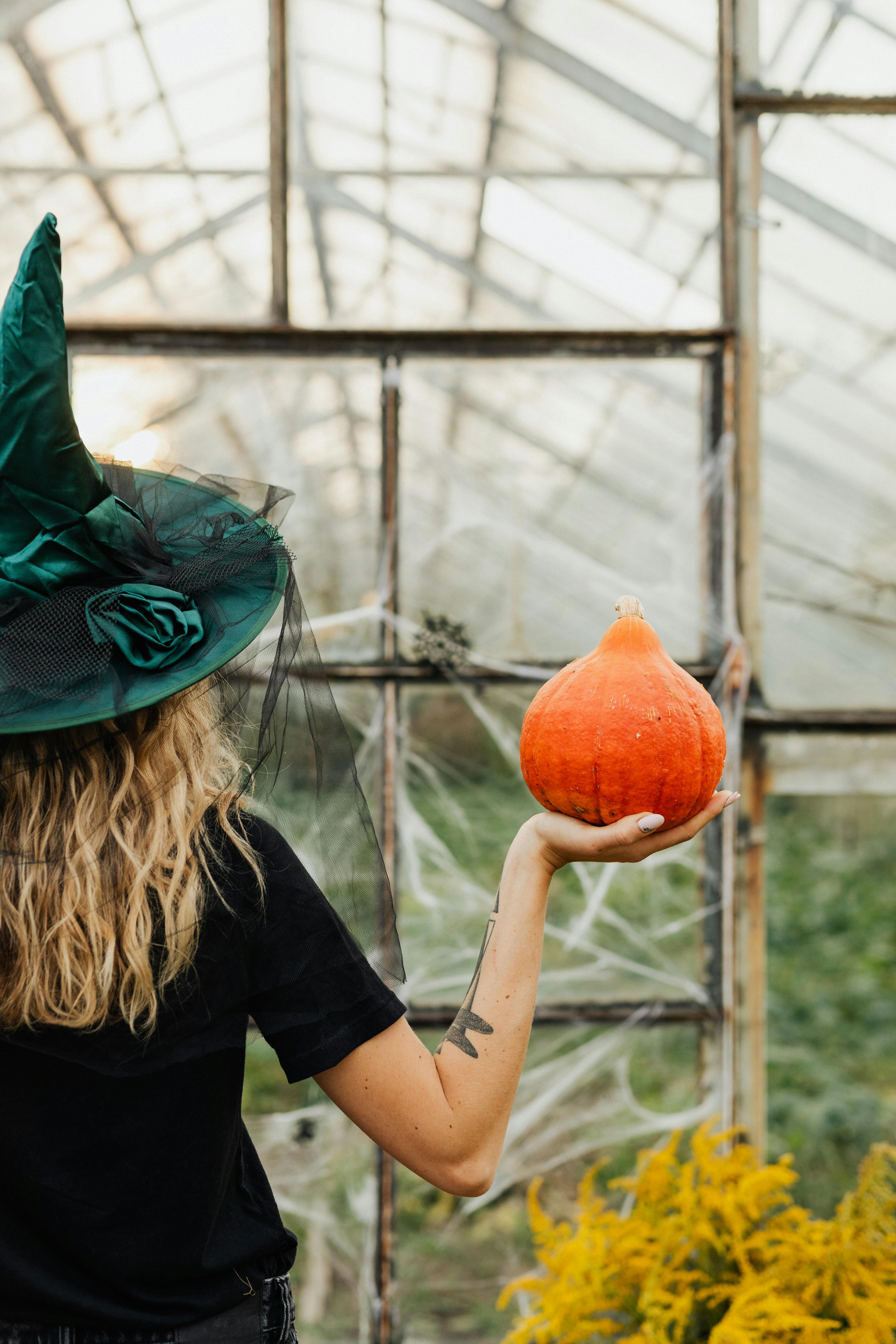 一名女子身着女巫服装，在乡村温室里手捧南瓜，散发着万圣节的气息