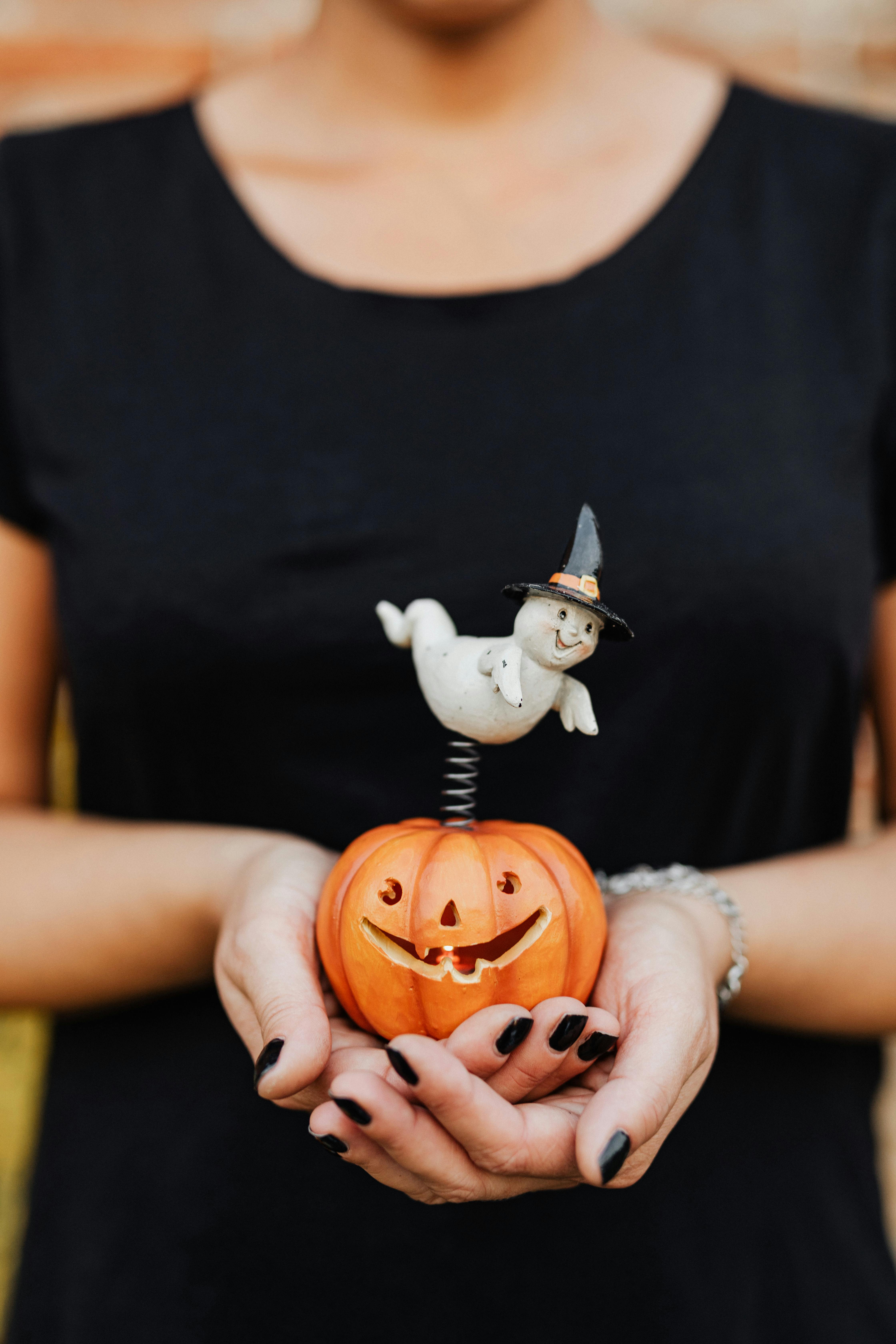 person holding a toy jack o lantern with a ghost