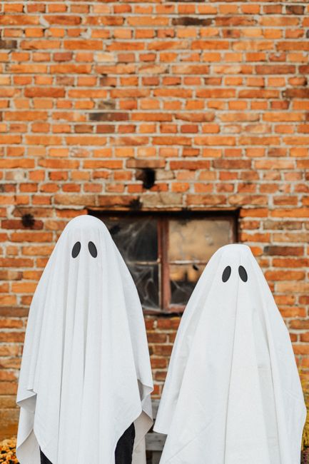 Two ghost costumes in front of a brick wall, perfect for Halloween themes.