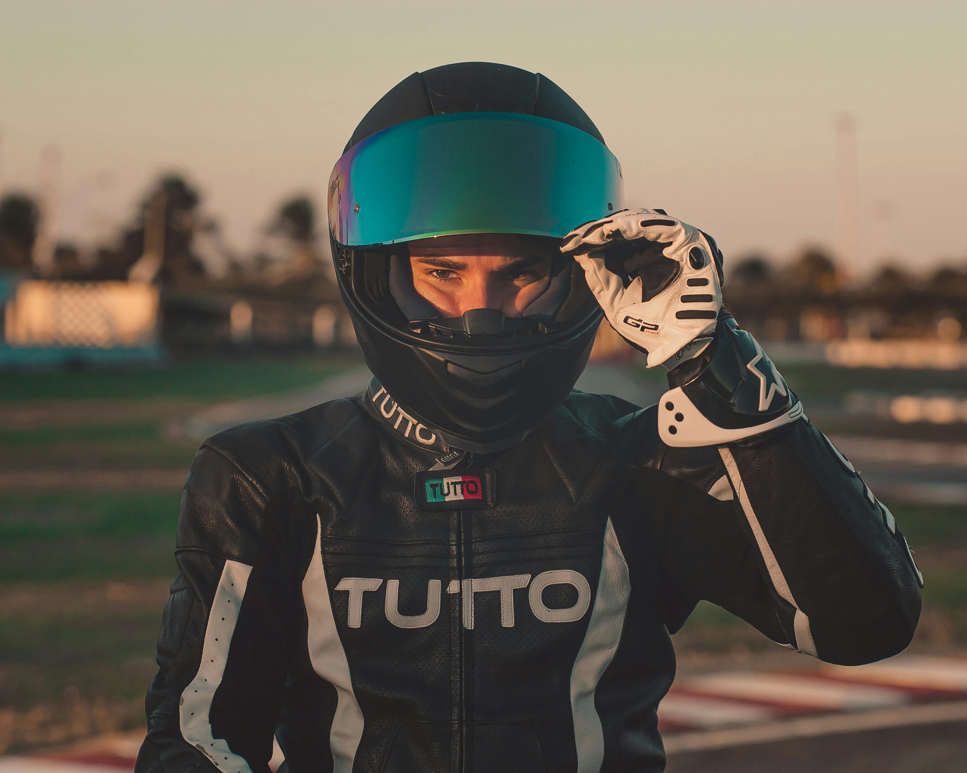 Motorcyclist wearing a helmet and leather suit adjusting visor at raceway.