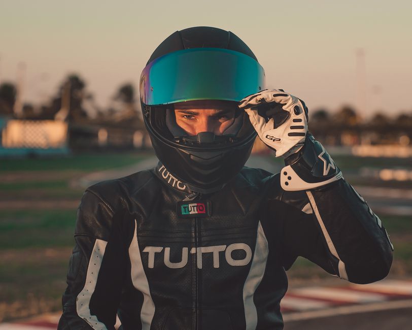 Motorcyclist wearing a helmet and leather suit adjusting visor at raceway.