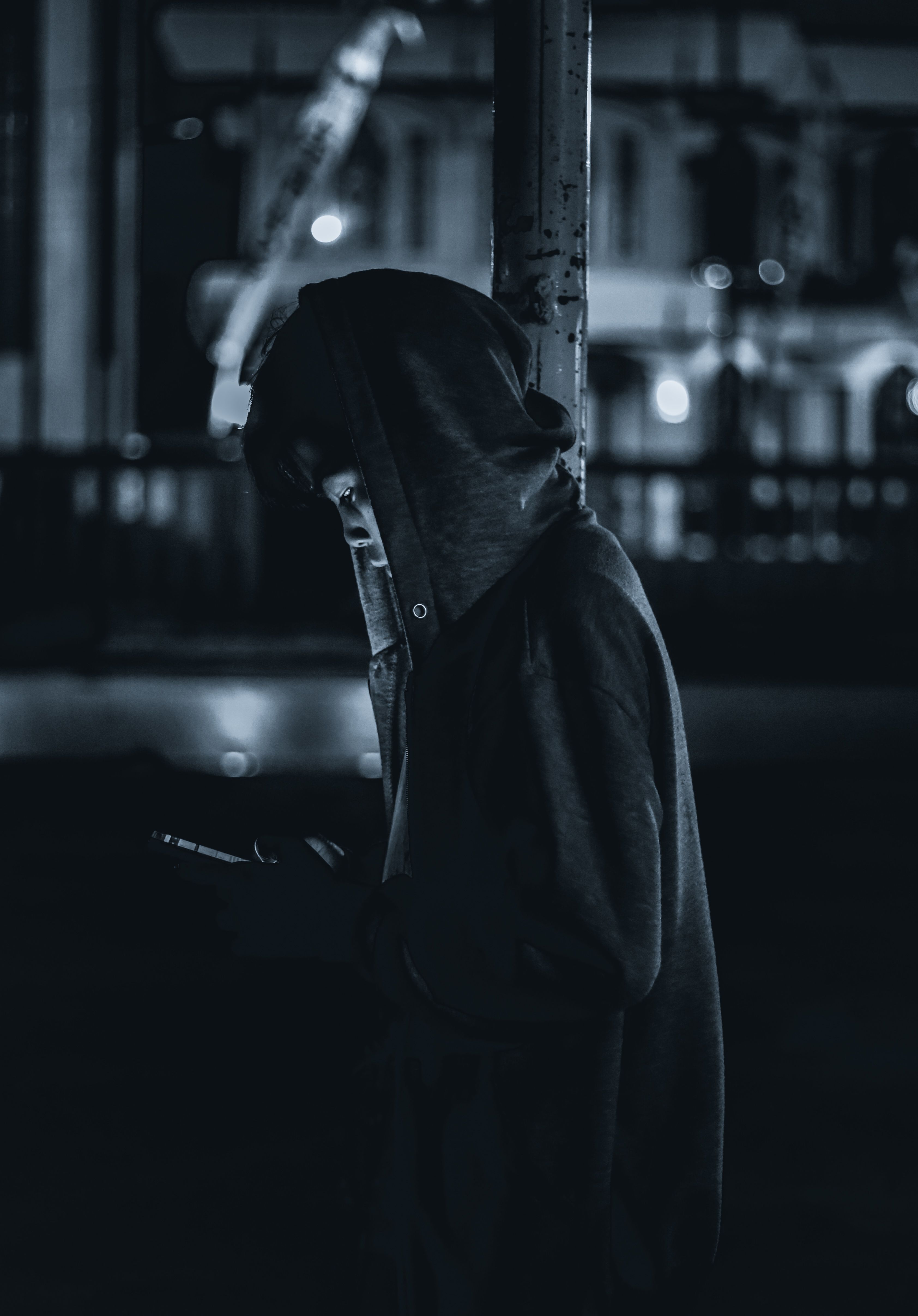 Silhouette of a person with a hoodie, illuminated by a phone at night, capturing urban mystery.