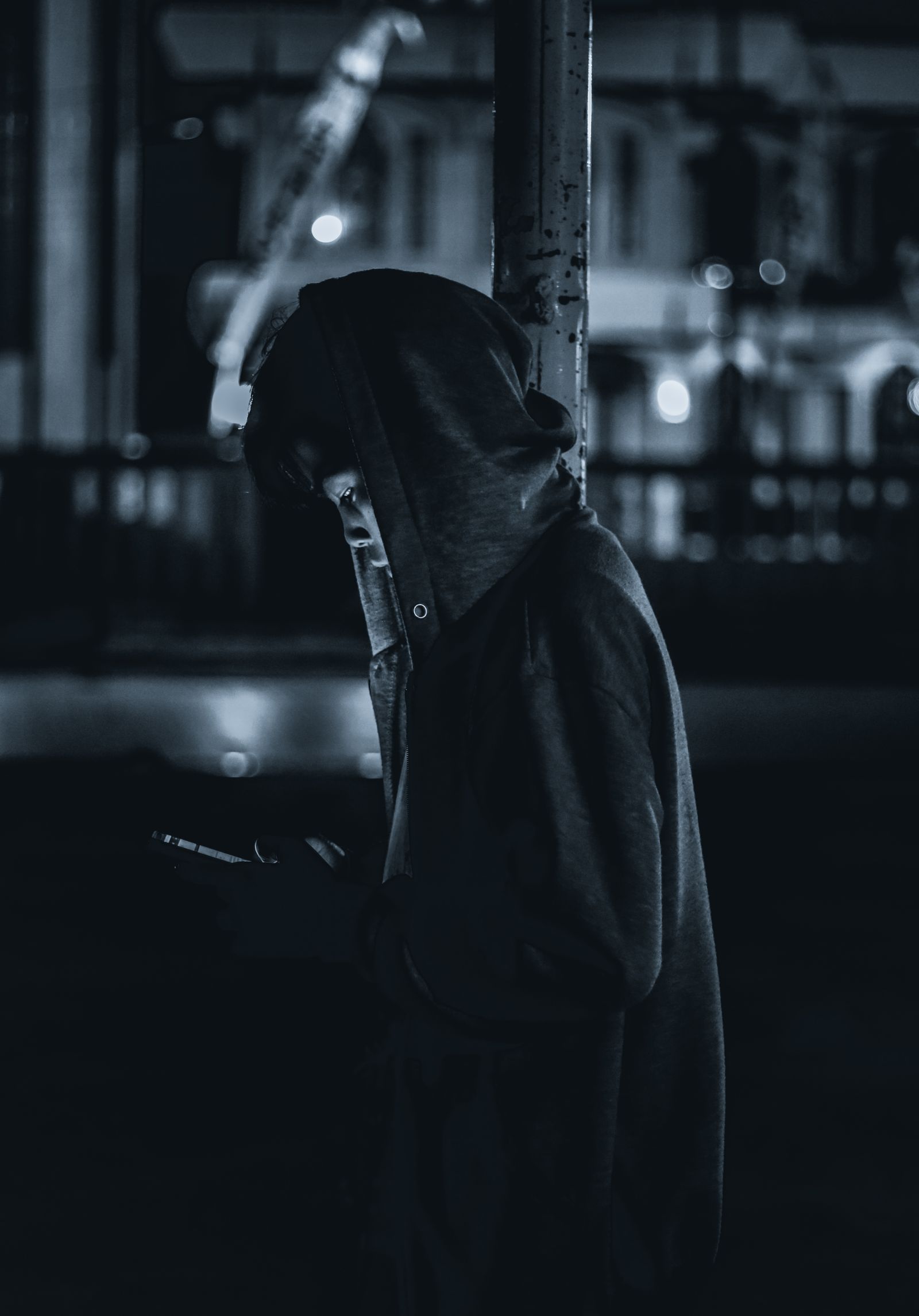 Silhouette of a hooded person with face lit by smartphone screen at night.