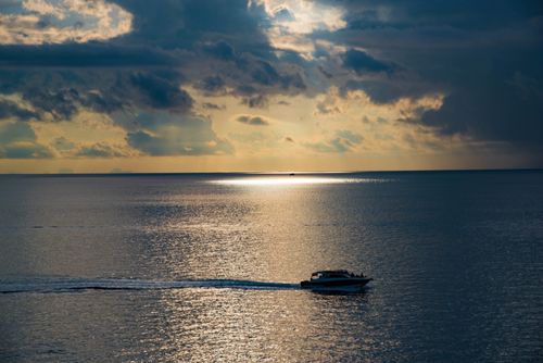 Free A serene boat sailing on a calm sea under a dramatic cloudy sky at sunset. Stock Photo