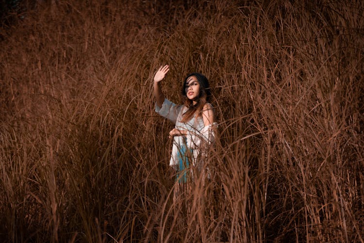 Young Woman Standing In Grassy Hill With Raised Hand