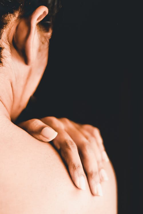 Back view of crop naked female touching shoulder with hand on black background