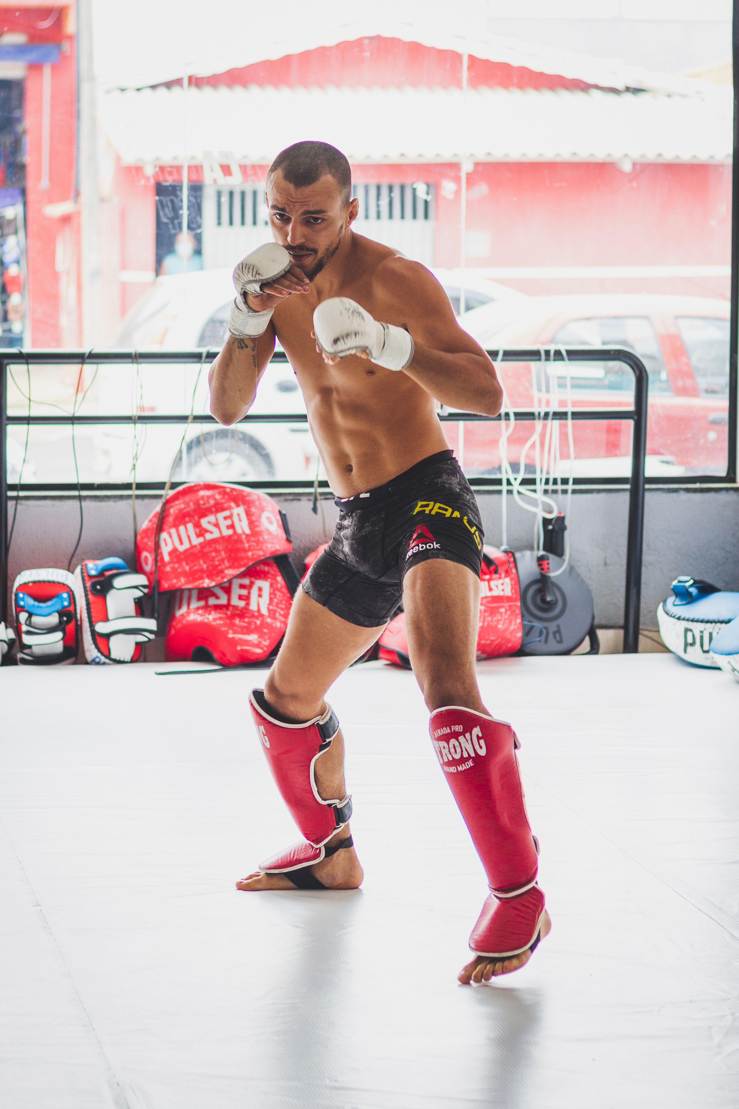 Male MMA fighter in a fighting stance during training indoors with gloves and shin guards.