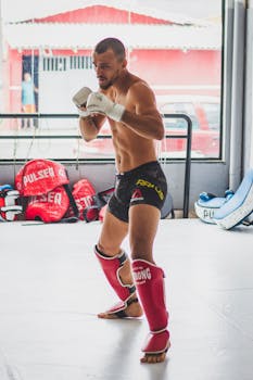 Young male fighter practicing martial arts in gym, wearing gloves and shin guards.