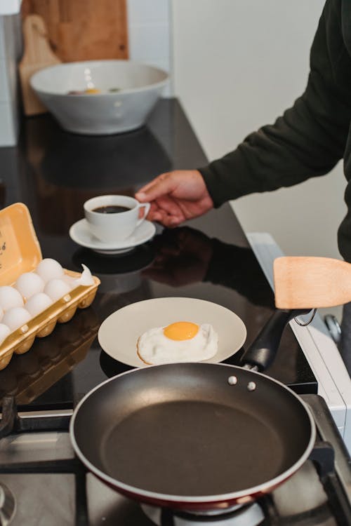 Free Crop anonymous person preparing delicious breakfast with fried egg and cup of aromatic coffee at home Stock Photo