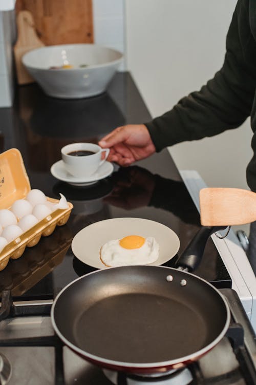 Crop anonymous person preparing delicious breakfast with fried egg and cup of aromatic coffee at home