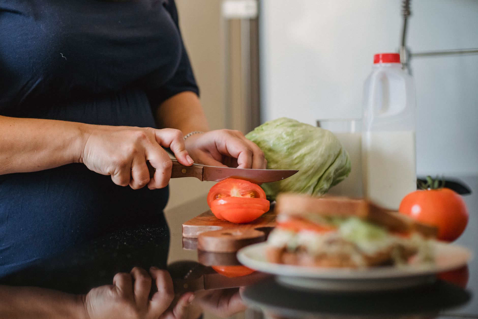 Crop unrecognizable female in casual clothes slicing fresh tomatoes while preparing healthy sandwiches in kitchen at home in daylight