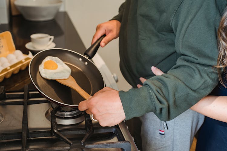 Man Preparing Fried Egg In Pan In Kitchen At Home