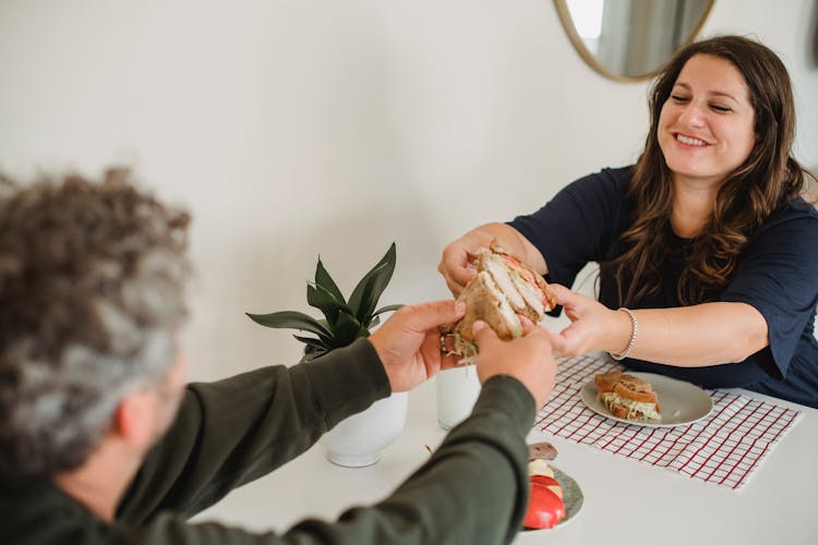 Happy Couple Eating Tasty Sandwiches At Home