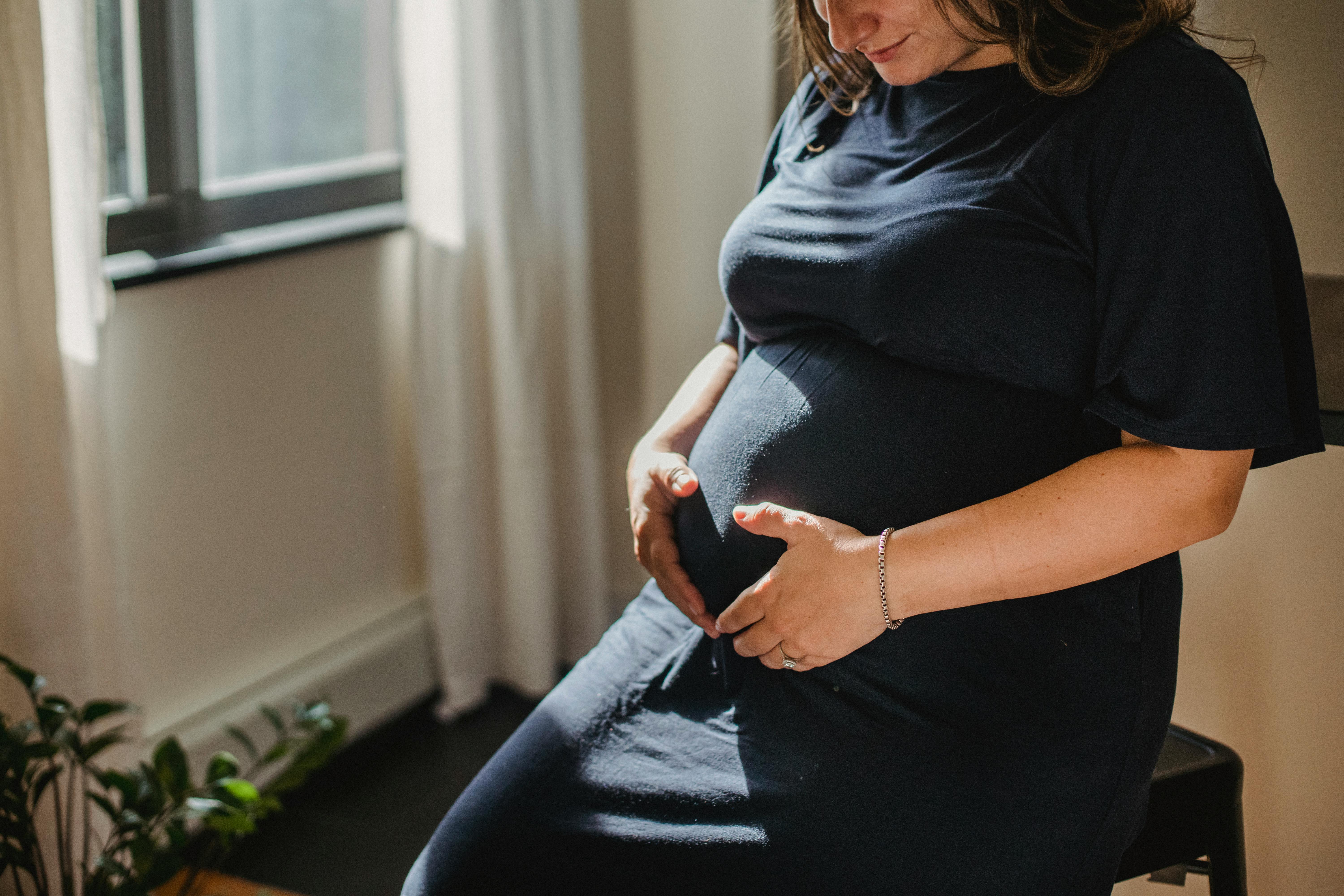 calm pregnant female touching belly at home in sunlight