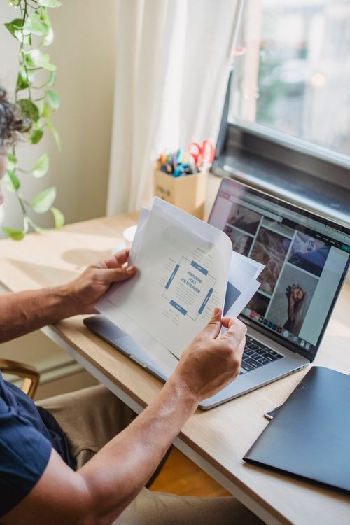Free Crop anonymous male worker sitting at table while working with documents and on laptop with internet access Stock Photo
