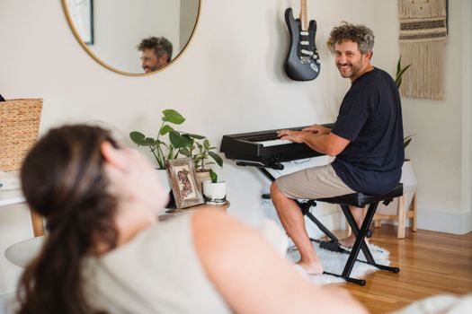 Loving adult male with beard and curly gray hair at wife while playing piano in cozy living room