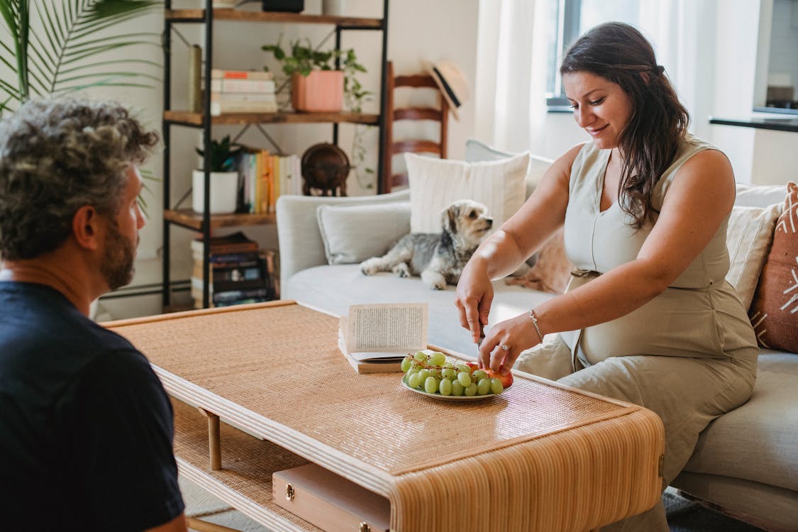 Cheerful pregnant woman serving fruit for man