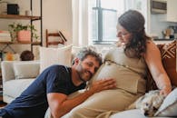 快乐的年轻孕妇轻抚着狗，而留着大胡子的丈夫则用脸颊贴着她的肚子