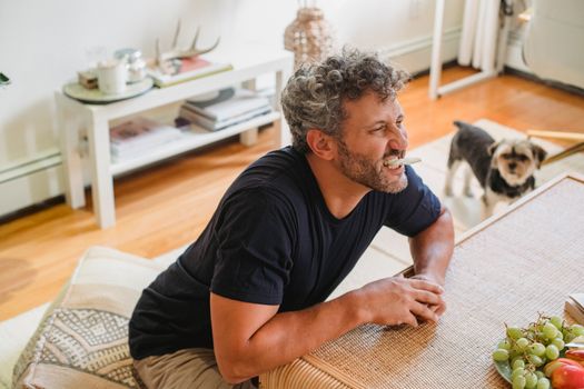 Cheerful adult male with beard and grey curly hair making faces with piece of apple in teeth