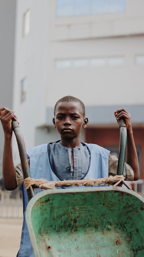 Pensive black child with wheelbarrow by modern building