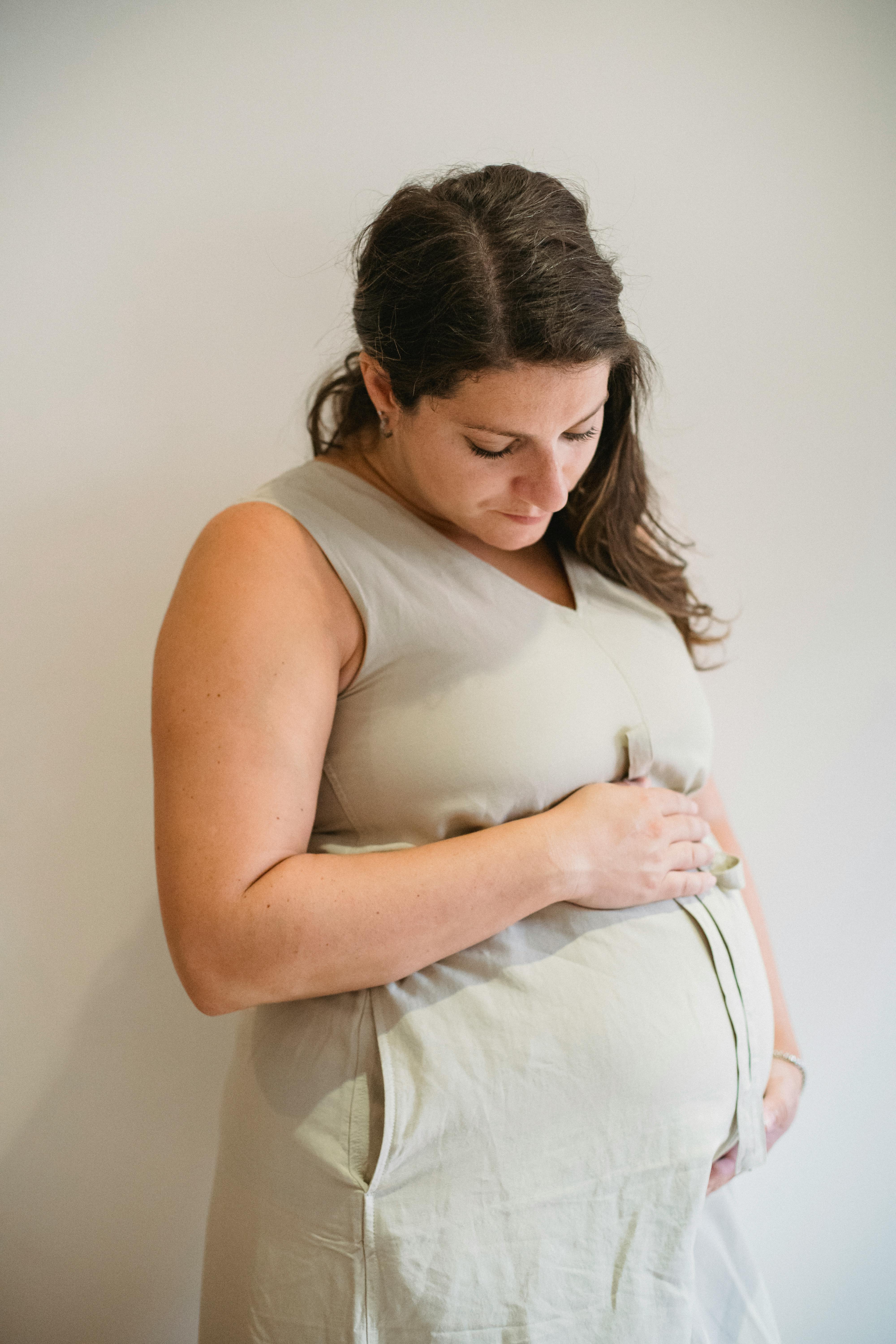 young pregnant woman looking down on belly against white background