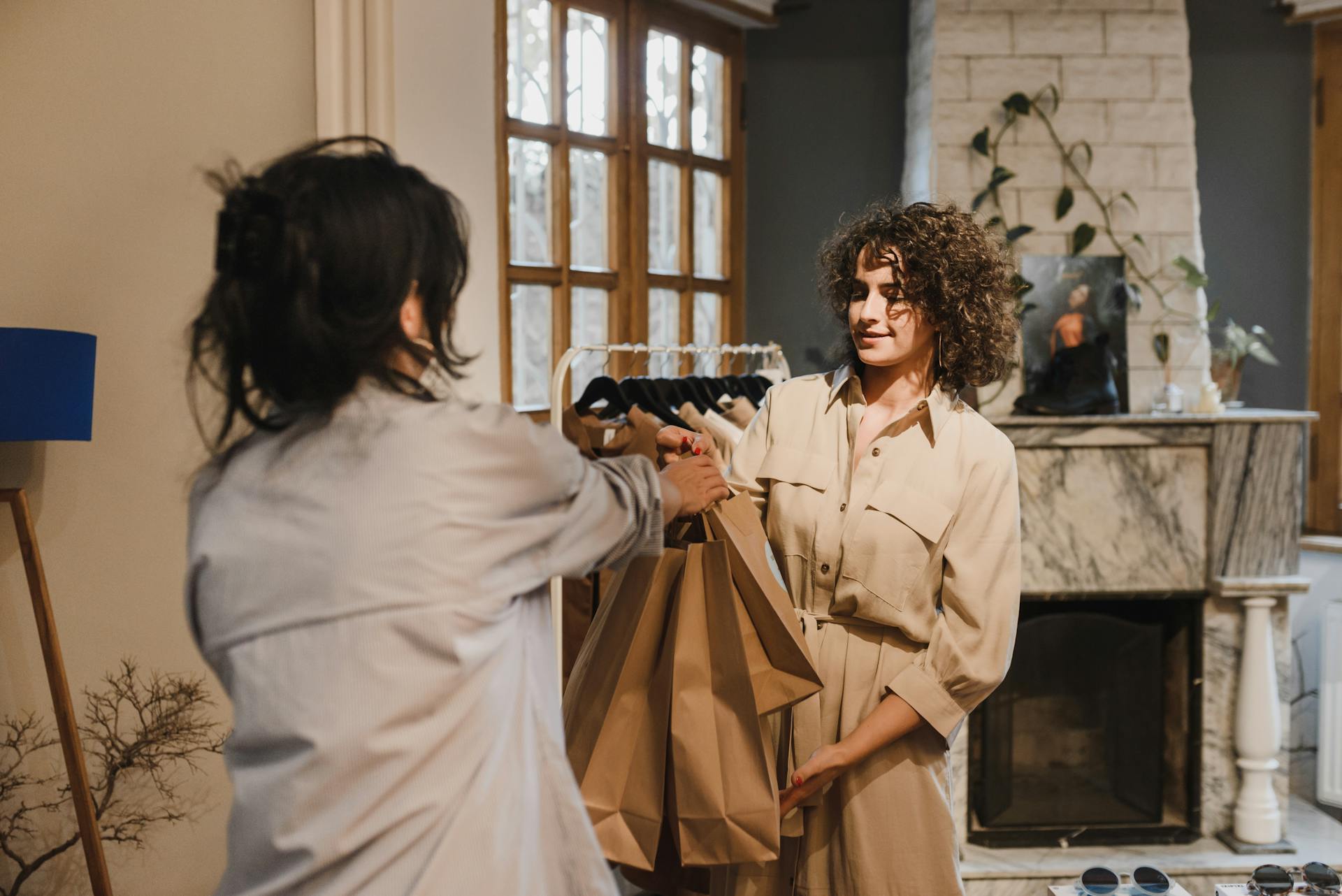 Two women in a boutique exchanging shopping bags with a cozy interior.