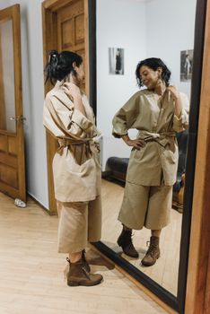 一位穿着米色和服和靴子的女人，正在室内对着镜子欣赏自己的倒影