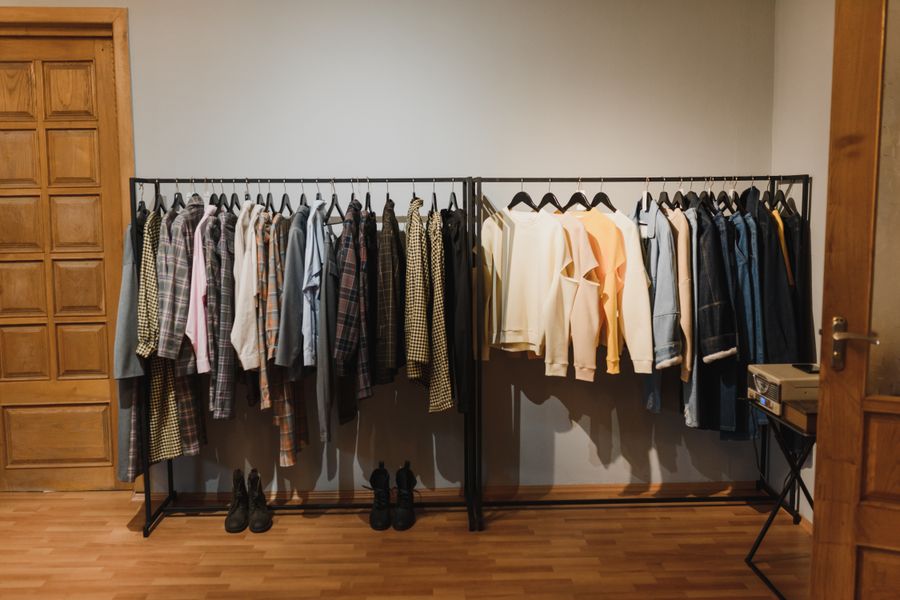A neatly arranged indoor clothing rack with various garments on hangers in a wooden-floored room.